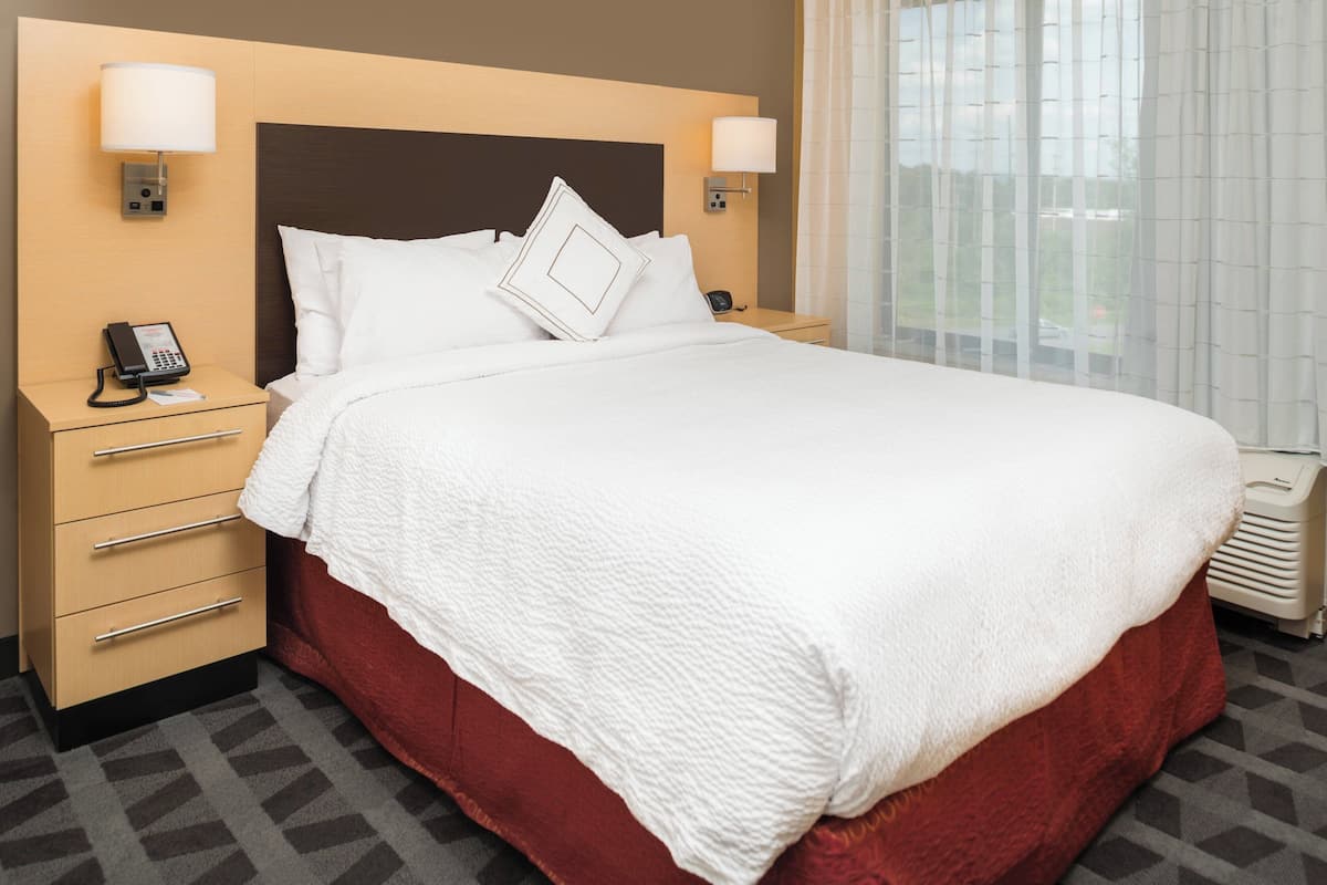A hotel room with a large bed, two bedside tables with lamps, a telephone, and a view of the outdoors through a window with curtains.