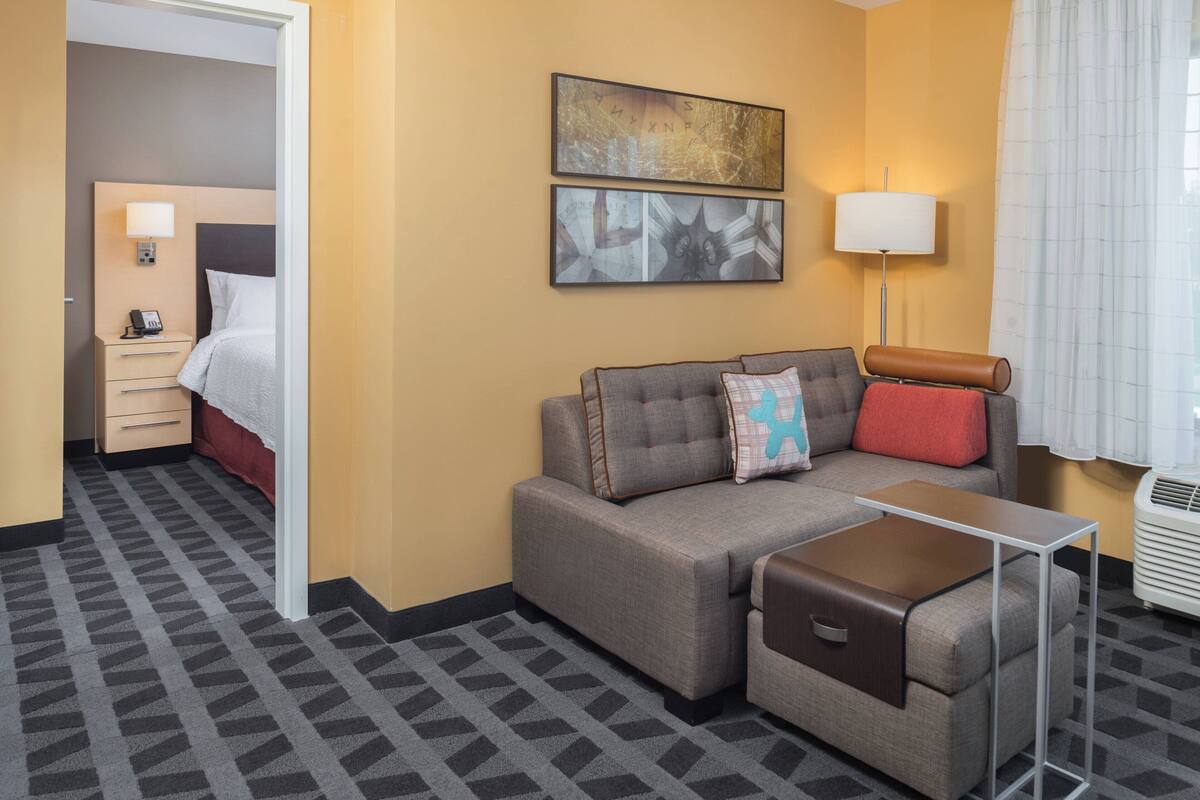 A hotel room with a sofa, a small table, a lamp, and a bed.