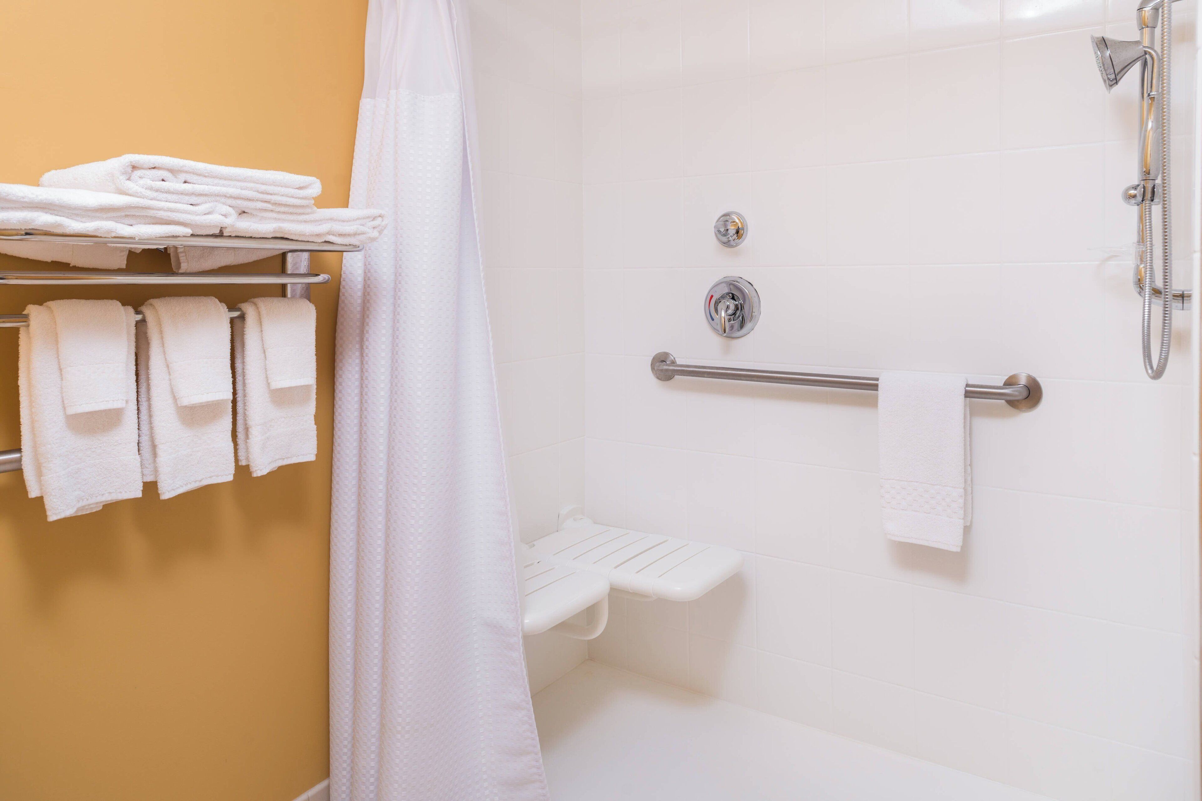 A bathroom with a shower, a toilet, and a towel rack with folded towels.