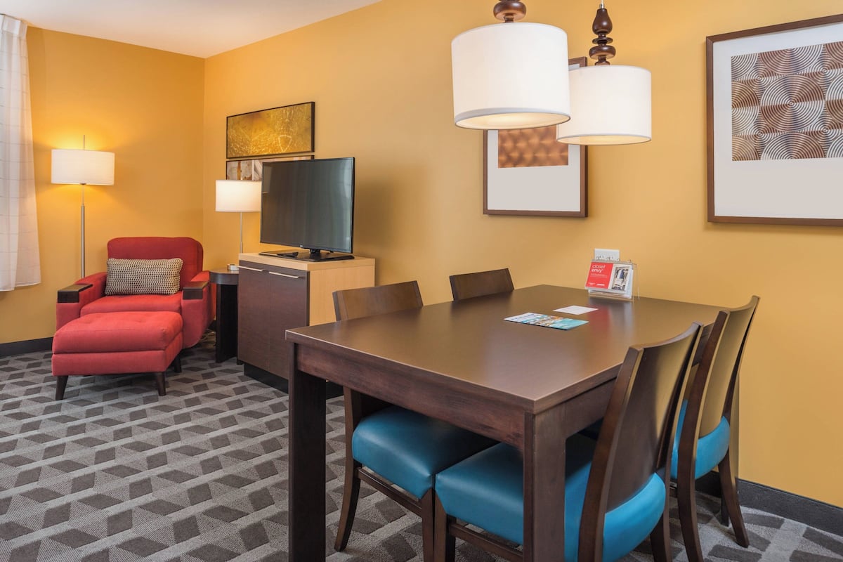 A hotel room with a dining table, chairs, a television, and a sofa.