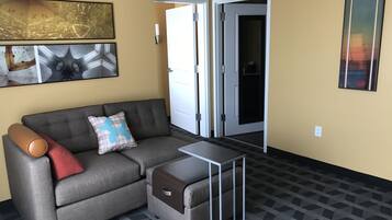 A modern living room with a grey sofa, a small table, and a door leading to a dark room.