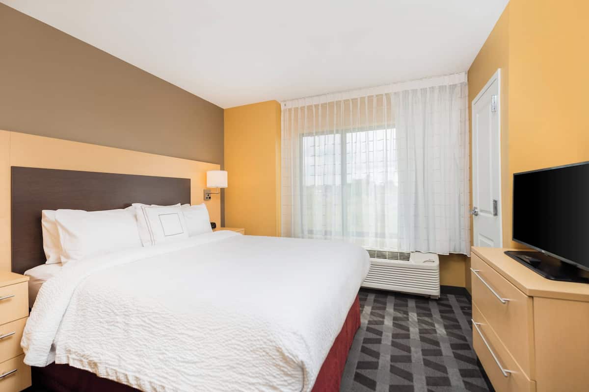 A hotel room with a large bed, a television, a desk, and a window with curtains.