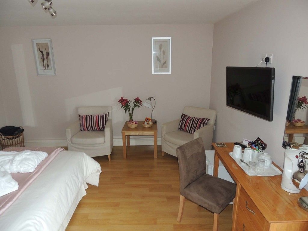 Habitación de hotel con cama, dos sillones, una mesita con flores, televisor y estación de café.