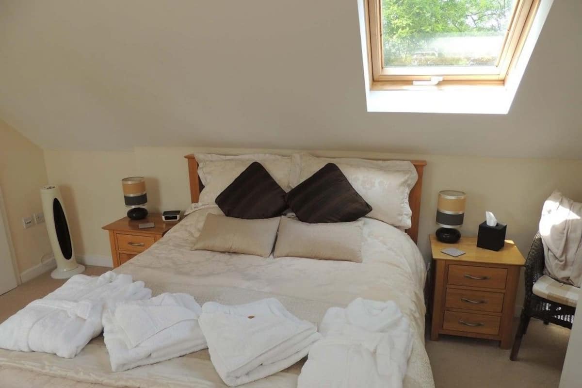 A bedroom with a bed, two bedside tables, a window, and a skylight.