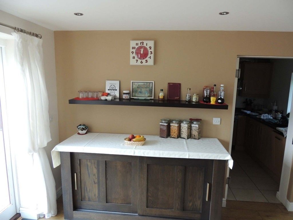 A kitchen with a wooden cabinet, a white countertop, and shelves with jars and a clock.