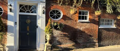 A traditional building with a dark blue door, a white entrance with a sign reading "Harmondsworth Hall," and brick walls with hanging plants.