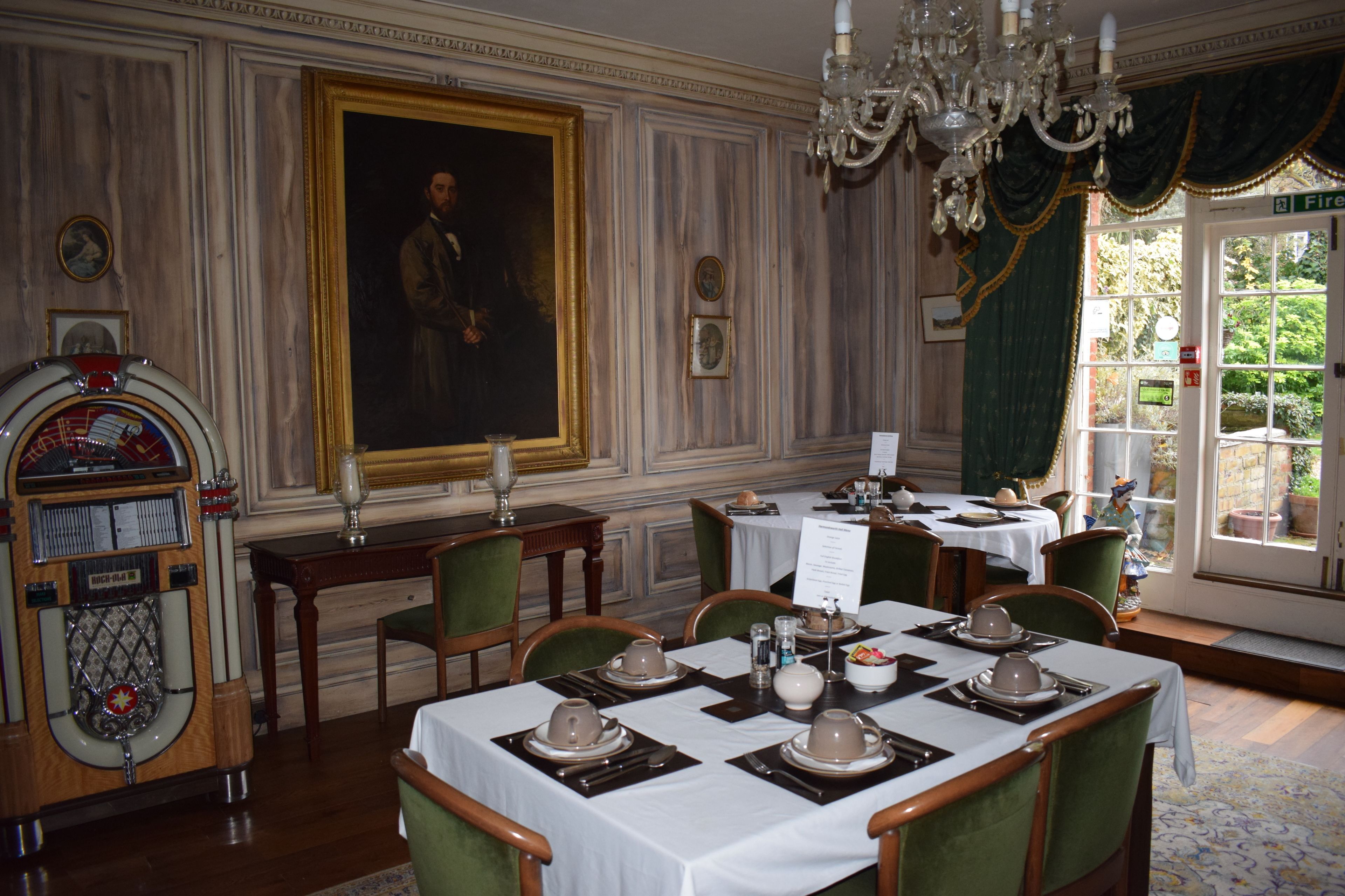 A dining room with tables set for a meal, a vintage jukebox, and a large portrait on the wall.