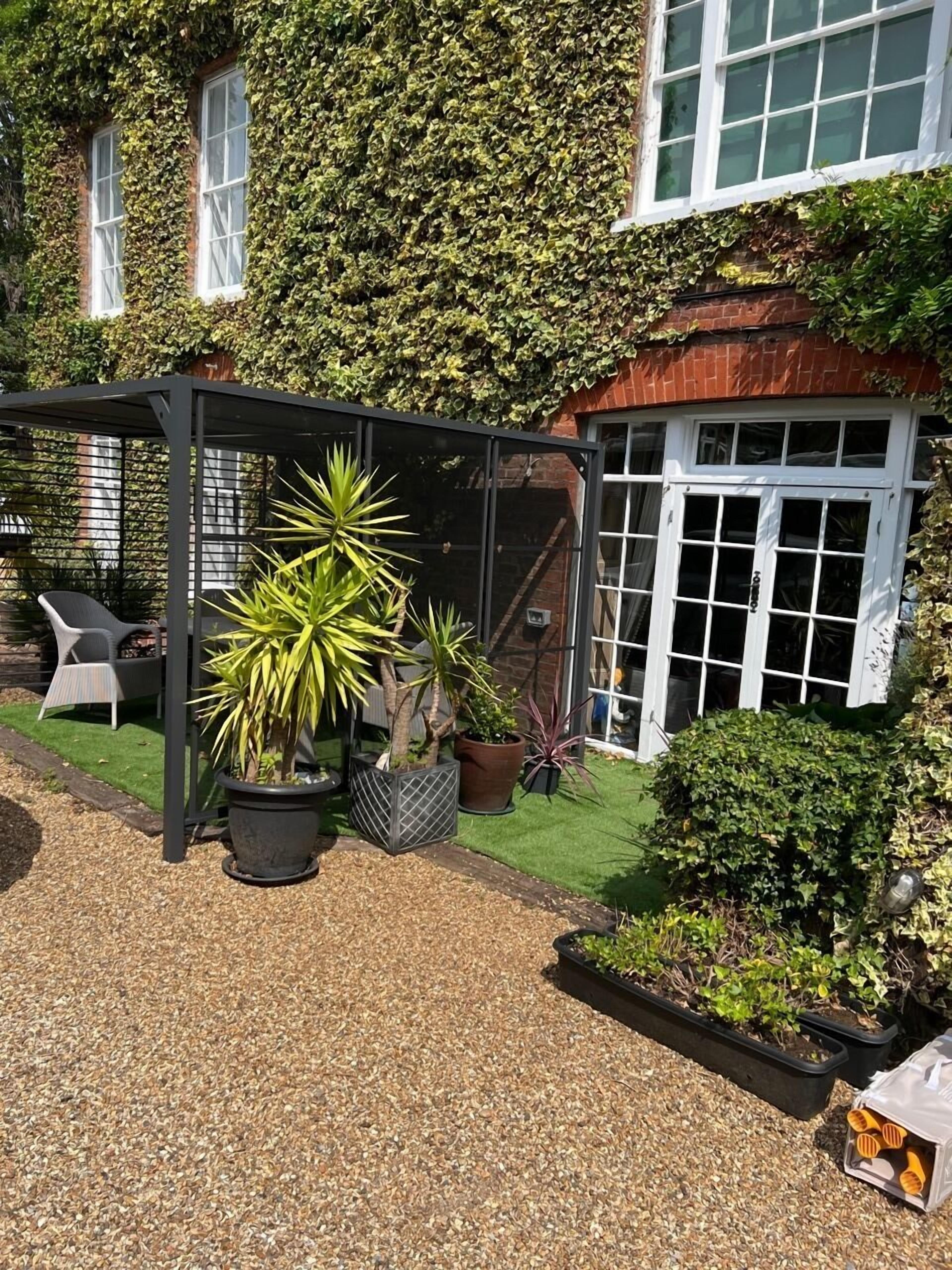 A garden with potted plants, a pergola, and a house with ivy-covered walls.