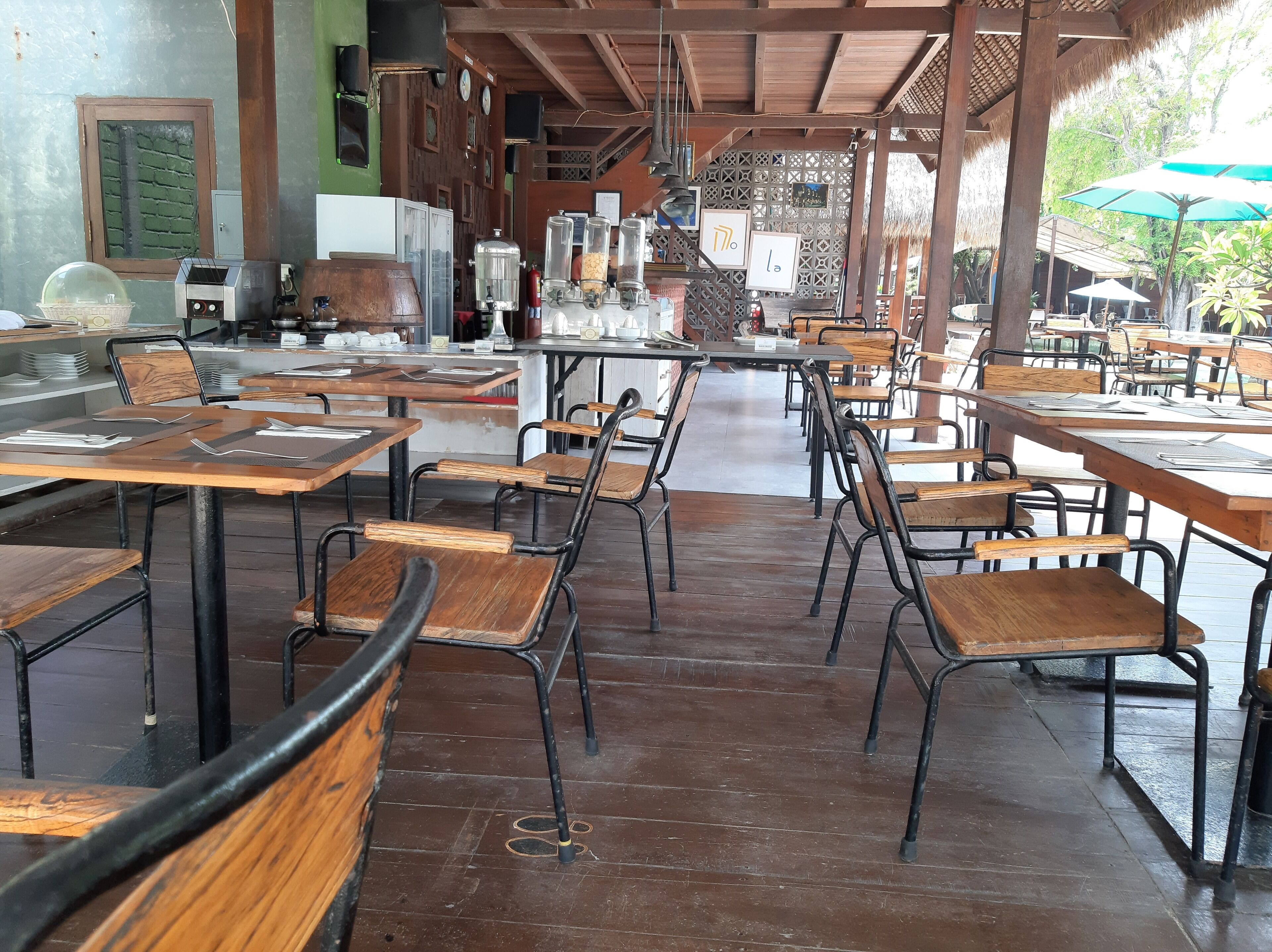 Un café en plein air avec des tables et des chaises en bois, un toit de chaume et une vue sur les environs.
