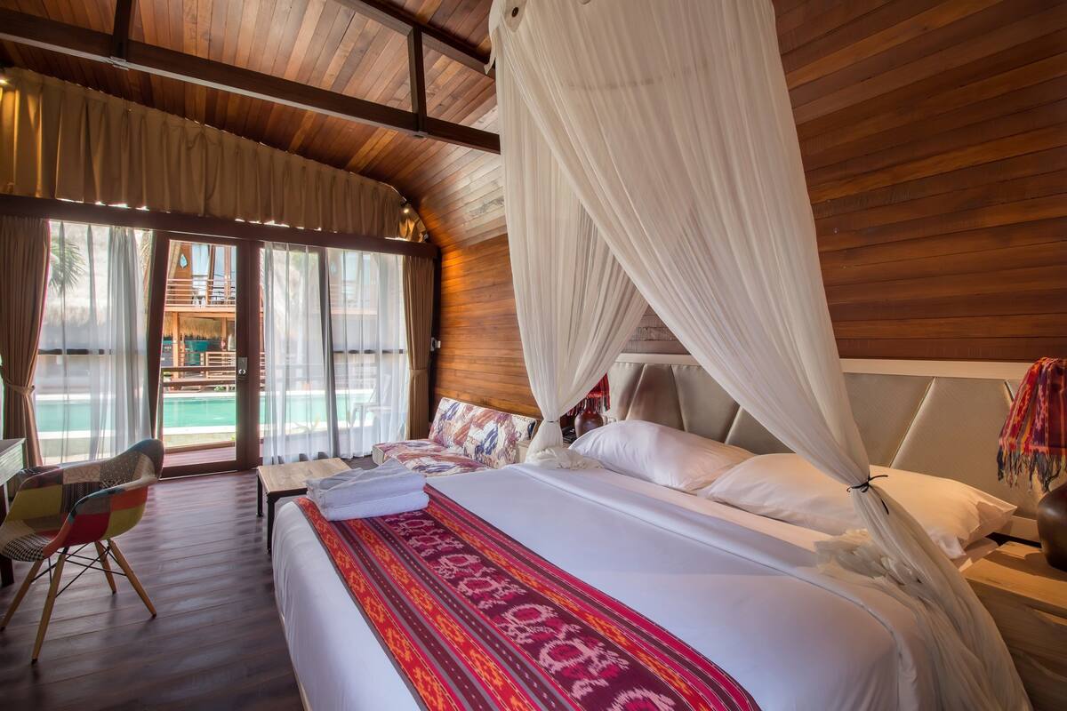 Une chambre avec un grand lit, une chaise et une vue sur l’extérieur.
