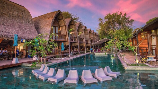 A resort with thatched-roof buildings, a swimming pool with lounge chairs, and a tropical garden setting.