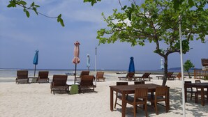 A beachside seating area with wooden tables and chairs, and several umbrellas.
