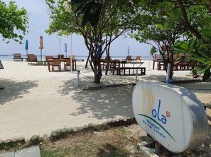 Un resort en la playa con sillones y mesas de madera, un cartel que dice 'Mola Resort' y vista al océano.