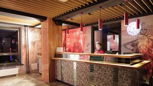 A reception area with a wooden reception desk, a clock, and a wall with a red tapestry. - Hotel Nine (Ulaanbaatar)