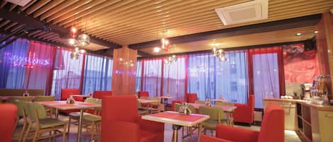 A restaurant with wooden ceiling slats, red and green chairs, and tables.