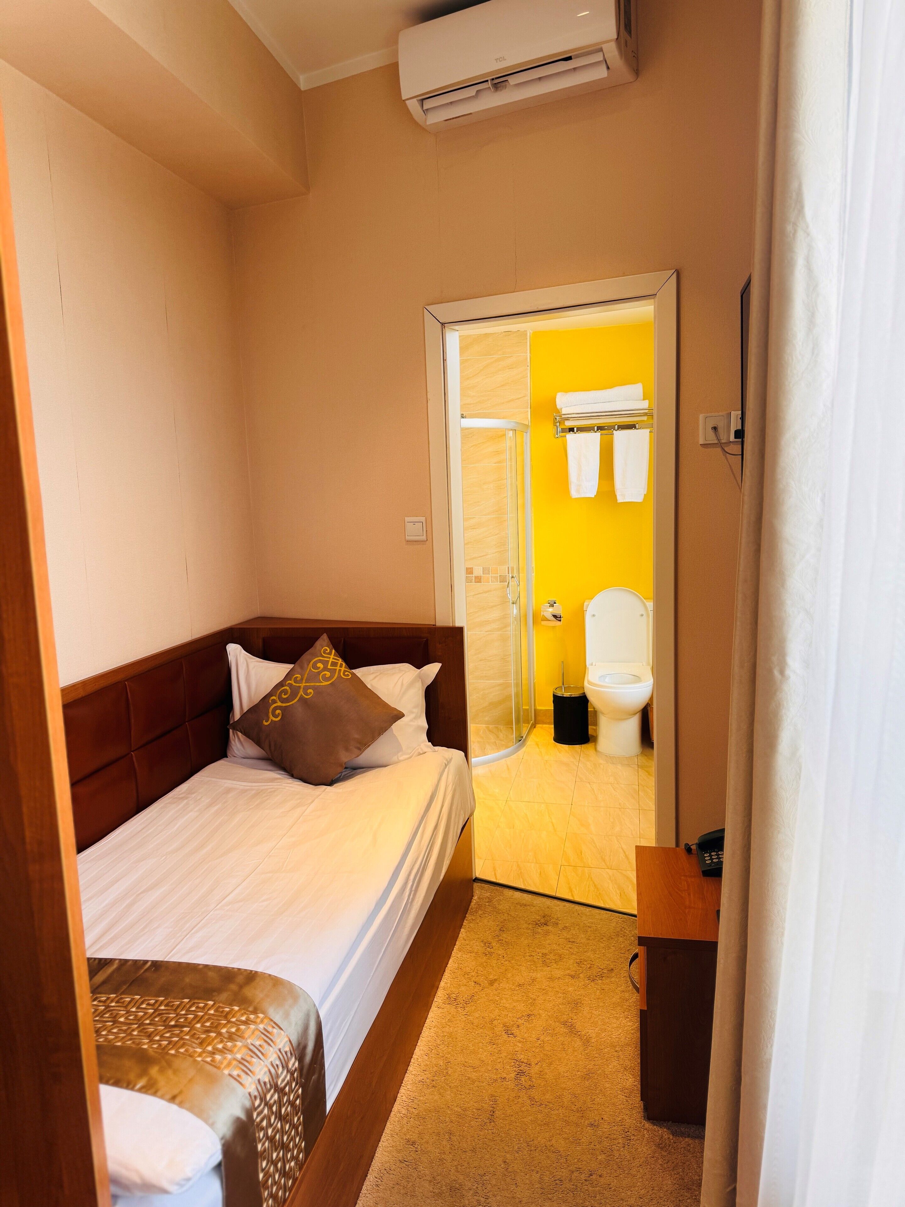 Ein Hotelzimmer mit einem Bett, einem Nachttisch, einer Klimaanlage und einem durch eine offene Tür einsehbaren Badezimmer.