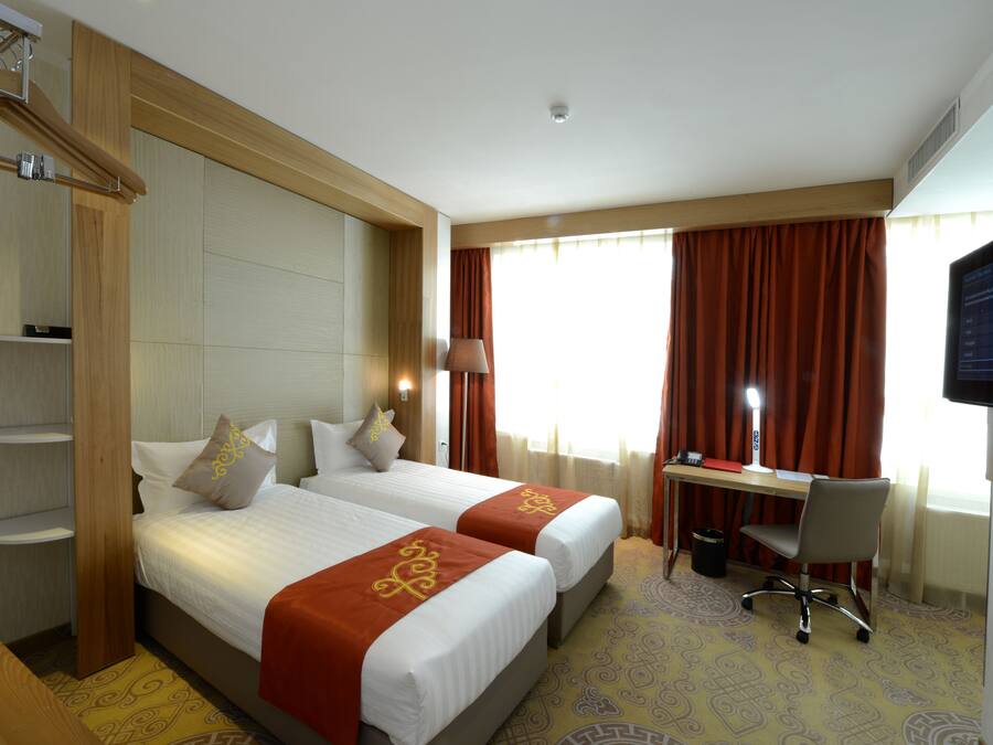 A hotel room with two beds, a desk, a chair, a TV, and a window with curtains.