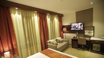 Habitación de hotel con cama, sofá, escritorio, televisor y espejo.