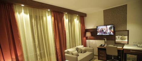 Habitación de hotel con cama, sofá, escritorio, televisor y espejo.