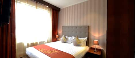 A hotel room with a large bed, a nightstand, a lamp, and a window with curtains.