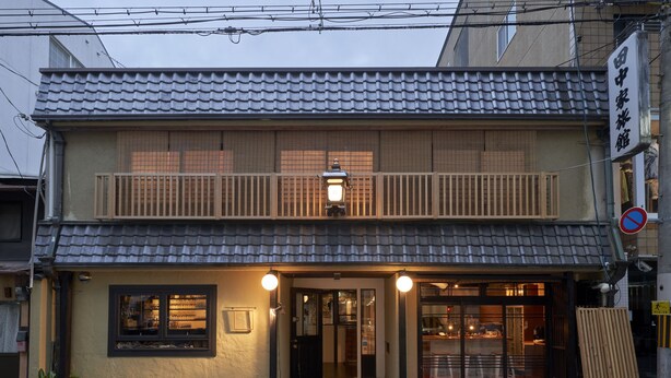 Ein traditionelles japanisches Gebäude mit einem Ziegeldach, einem hölzernen Balkon und einem Eingangsbereich mit einer Bank.