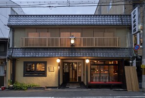 A traditional Japanese building with a tiled roof, a wooden balcony, and a front entrance with a bench. - HOTEL Clam Chowder (Kyoto)