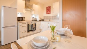 A modern kitchen with white appliances, a dining table set for two, and a vase with flowers. - Skyline Luxury Apartments (Stevenage)