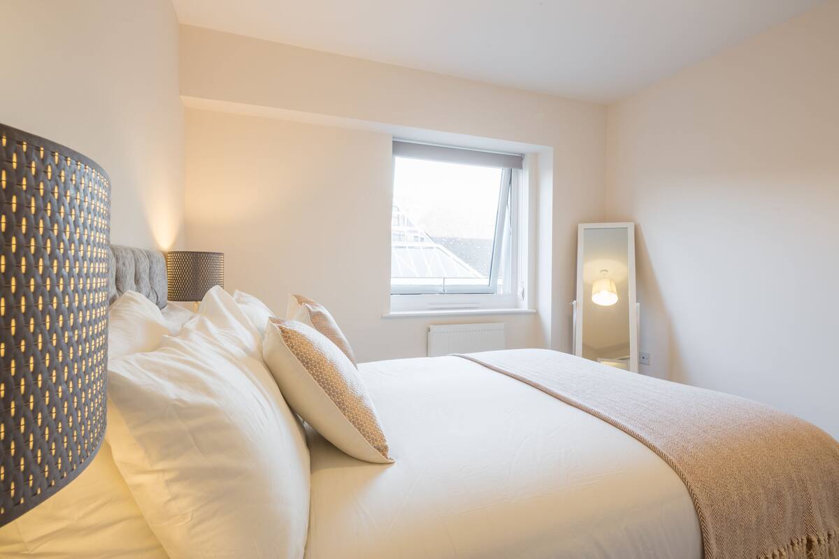 A bedroom with a large bed, a window with a view, a bedside lamp, and a mirror.
