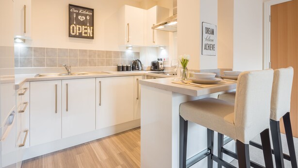 A modern kitchen with white cabinets, a bar stool, and a kitchen island. - Skyline Luxury Apartments (Stevenage)