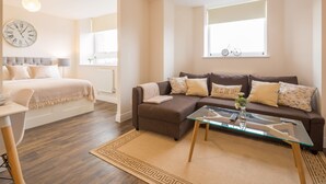 A modern living room with a sofa, coffee table, and a bed with a headboard. - Skyline Luxury Apartments (Stevenage)