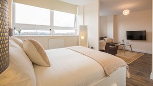 A modern hotel room with a large bed, a desk, a chair, and a TV mounted on the wall. - Skyline Luxury Apartments (Stevenage)