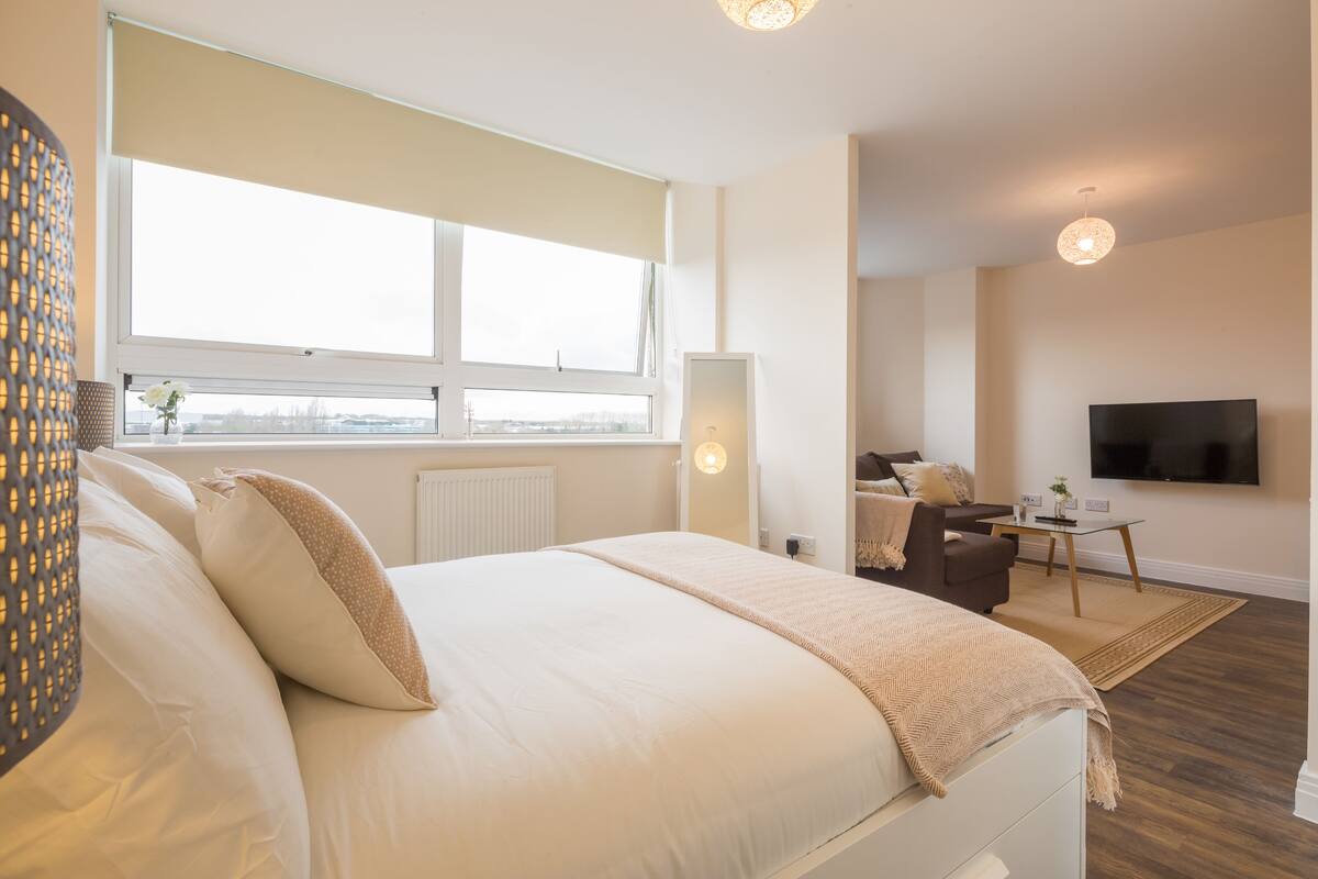 A modern hotel room with a large bed, a desk, a chair, and a TV mounted on the wall.
