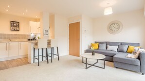 A modern living room with a grey sofa, a round coffee table, and a dining area with a white table and two chairs. - Skyline Luxury Apartments (Stevenage)