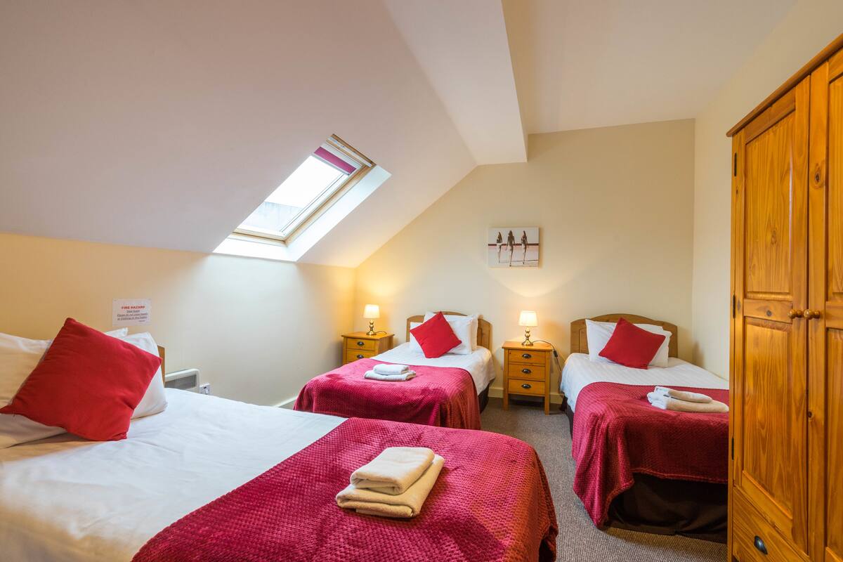 Ein Schlafzimmer mit zwei Betten, jeweils mit roter Bettdecke und weißen Kissen, einem Oberlicht und einem hölzernen Kleiderschrank.