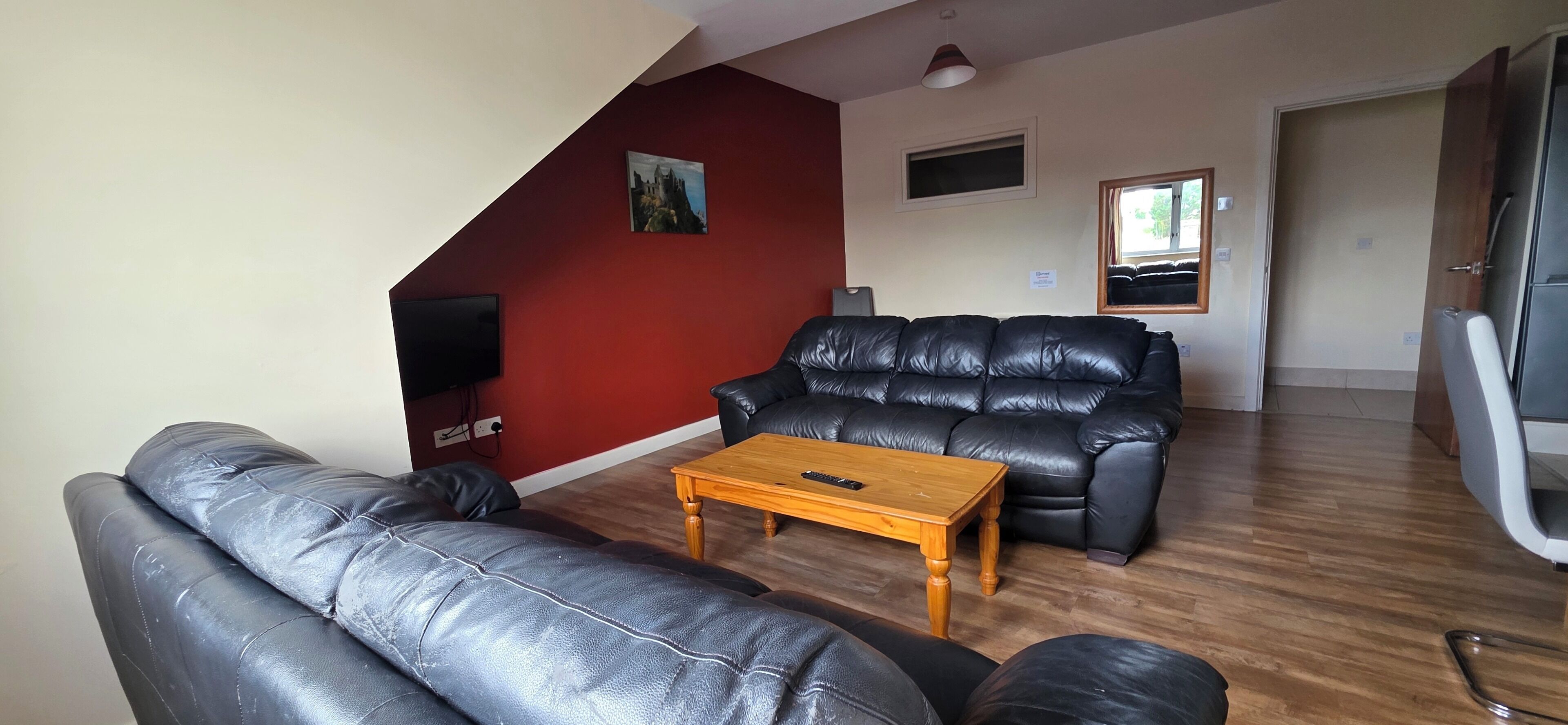 A living room with a black leather sofa, a wooden coffee table, and a red accent wall.