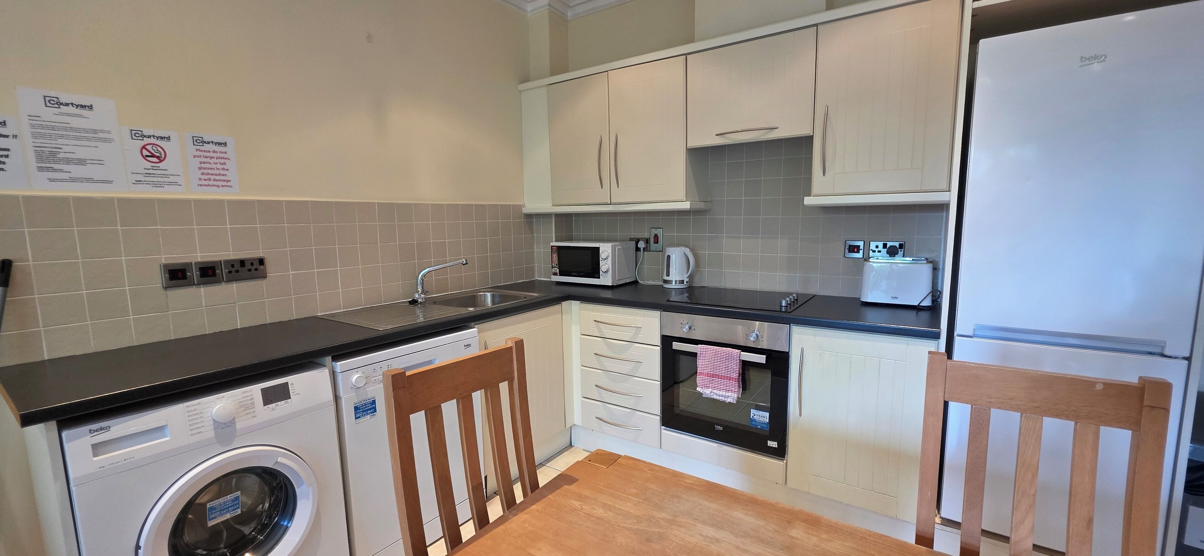 A compact kitchen with a washing machine, microwave, oven, and a refrigerator.