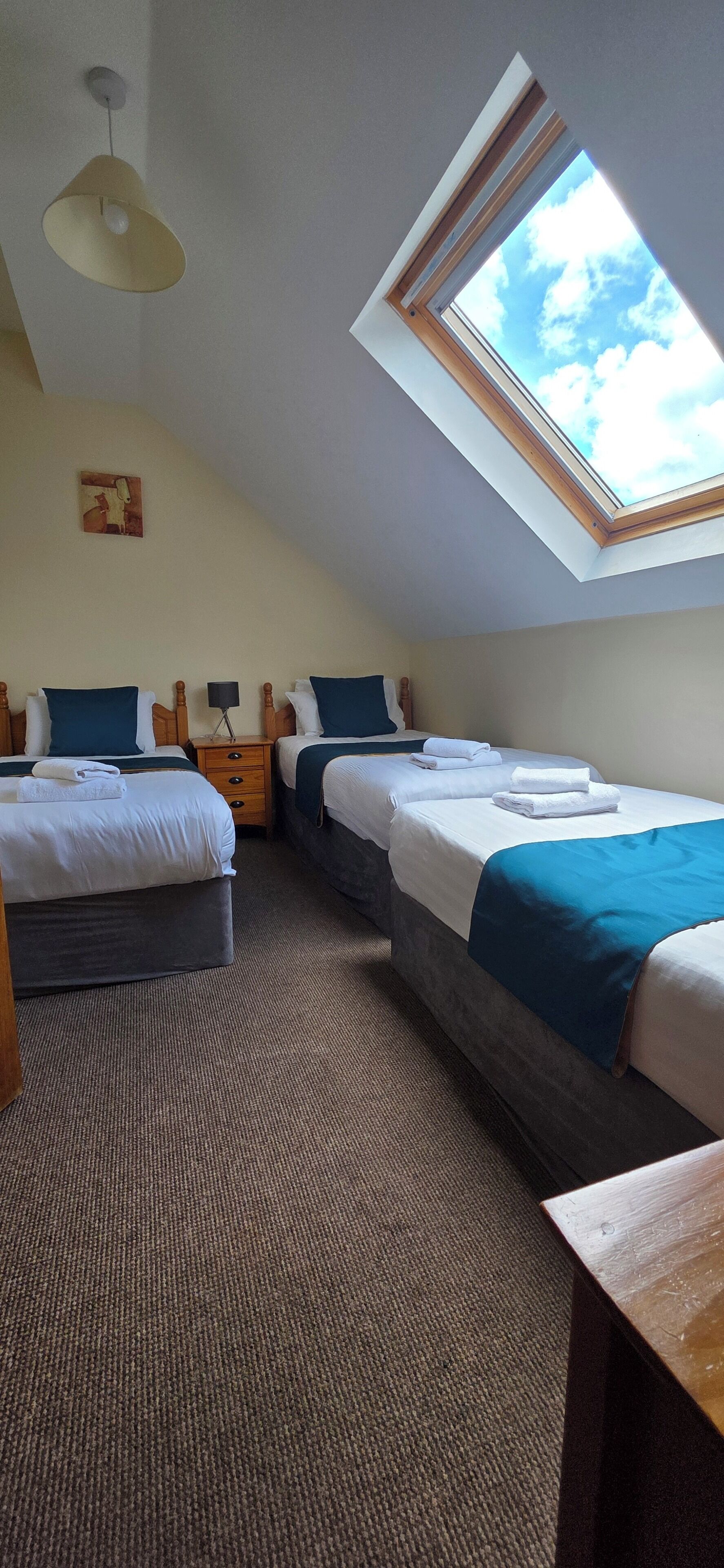 A room with two beds, a skylight, a ceiling fan, and a small table.