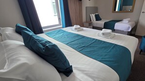 A hotel room with a large bed, a smaller bed, and a desk. There are towels on the beds and a mirror on the wall. - The Courtyard Apartments (Carrick-on-Shannon)
