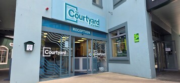 A building with a sign reading "The Courtyard Apartments" and a reception area visible through the glass doors.