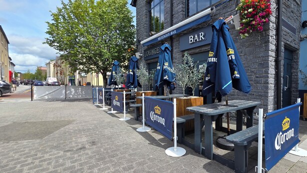 An outdoor seating area with tables and chairs, a bar, and a sign for 'MUKTAGHS BAR'. - The Courtyard Apartments (Carrick-on-Shannon)