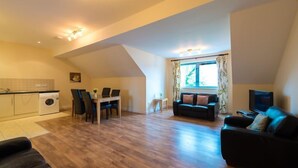 A compact living space with a dining area, a sofa, a TV, and a washing machine. - The Courtyard Apartments (Carrick-on-Shannon)
