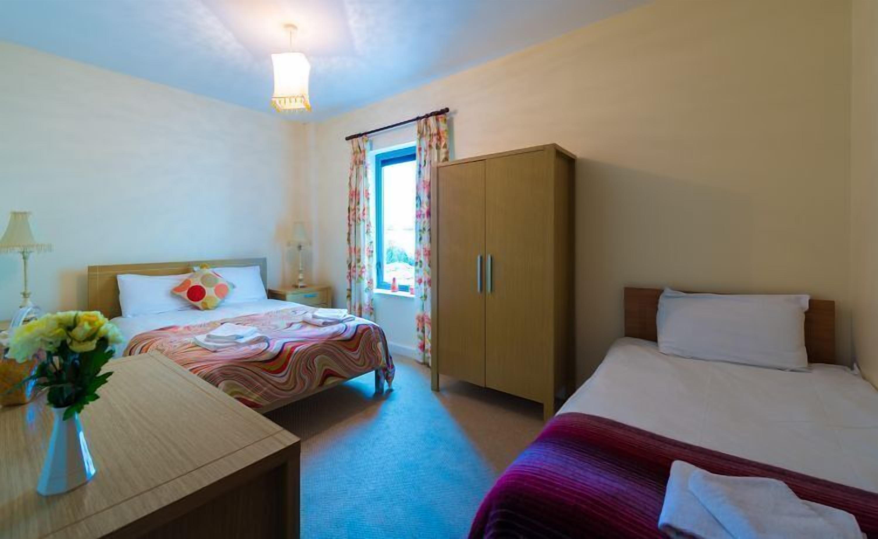 Camera d'albergo con due letti, un armadio in legno, una scrivania con una lampada e una finestra con tende.