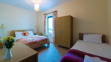 Camera d'albergo con due letti, un armadio in legno, una scrivania con una lampada e una finestra con tende.