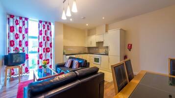 A compact living space with a sofa, a dining table, a TV, and a kitchenette.