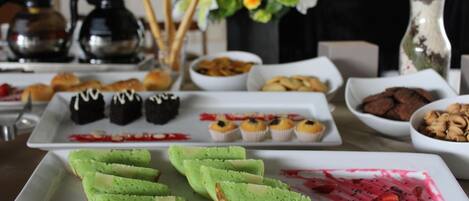 Una mesa de buffet con diversos alimentos, incluyendo pasteles verdes, cupcakes y un postre con fresas.