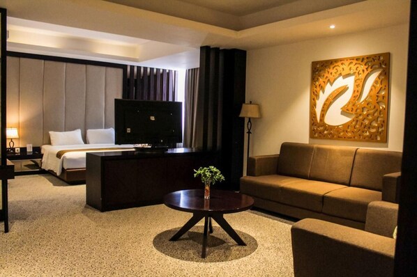 Una habitación de hotel con cama, televisor, sofá, mesa de centro y un adorno de pared.