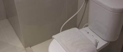 A white toilet with a towel on the seat and a bidet attachment.
