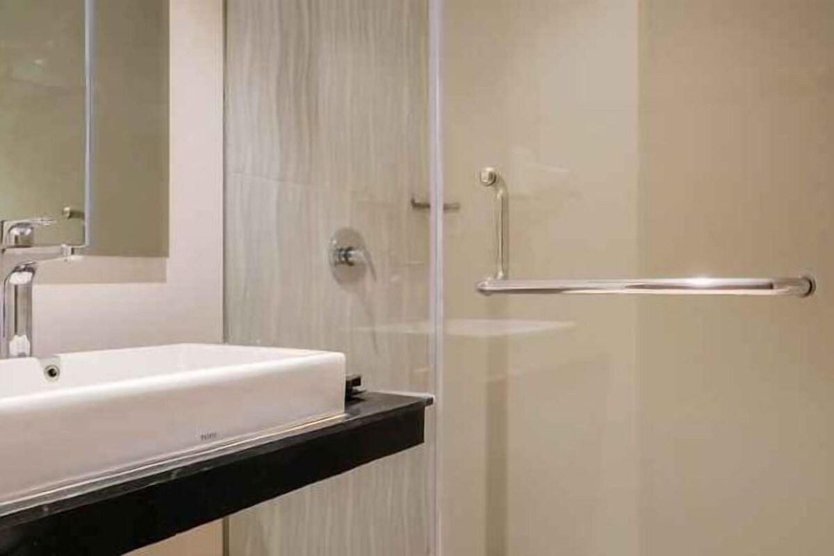 Un baño con lavamanos blanco, un espejo y cabina de ducha de cristal.