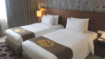 Habitación de hotel con dos camas, un papel tapiz estampado, una lámpara y un teléfono en la mesita de noche.