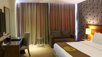 Habitación de hotel con cama, escritorio, silla, televisión y ventana con cortinas.